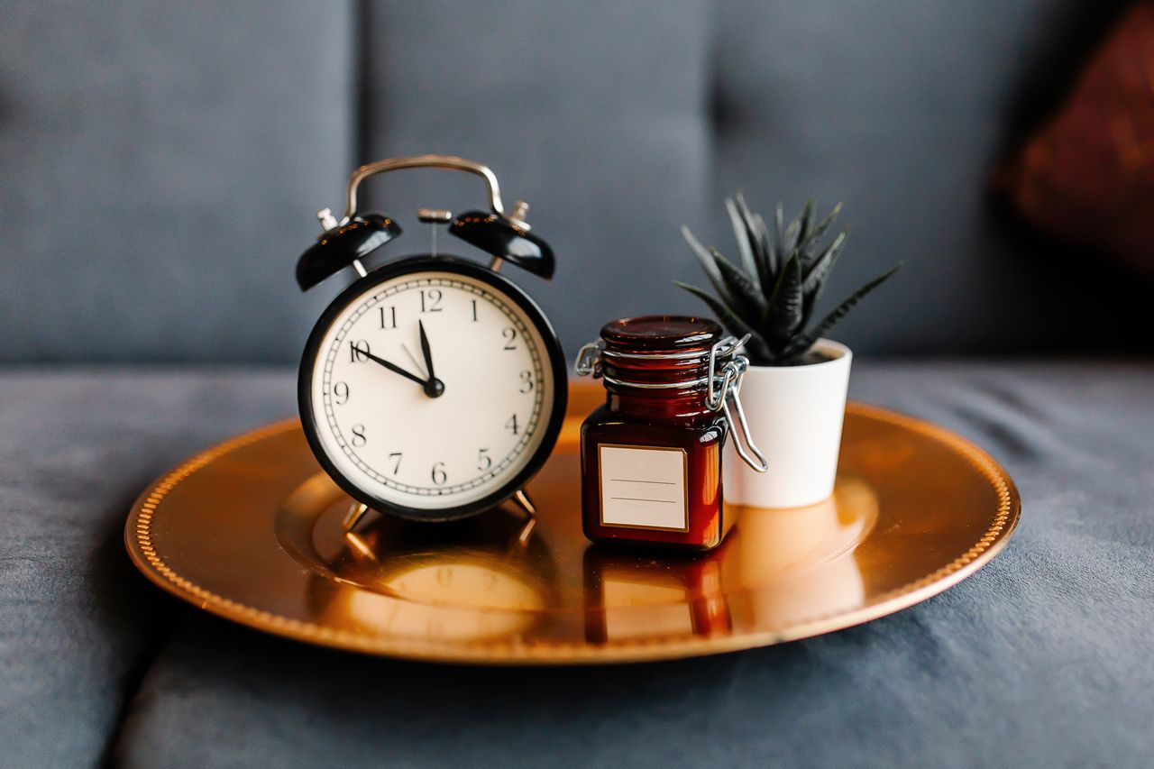 Aesthetic arrangement of a clock and jar on a golden tray with a potted plant.